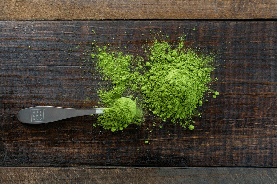 Measuring Spoon Full of Green Kratom Powder Next to Pile of Green Kratom Powder on Wooden Table