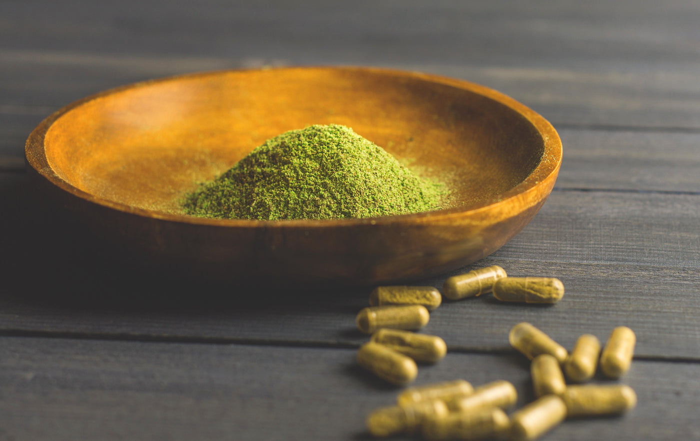a bowl of green kratom powder next to capsules|kratom powder on a black plate|